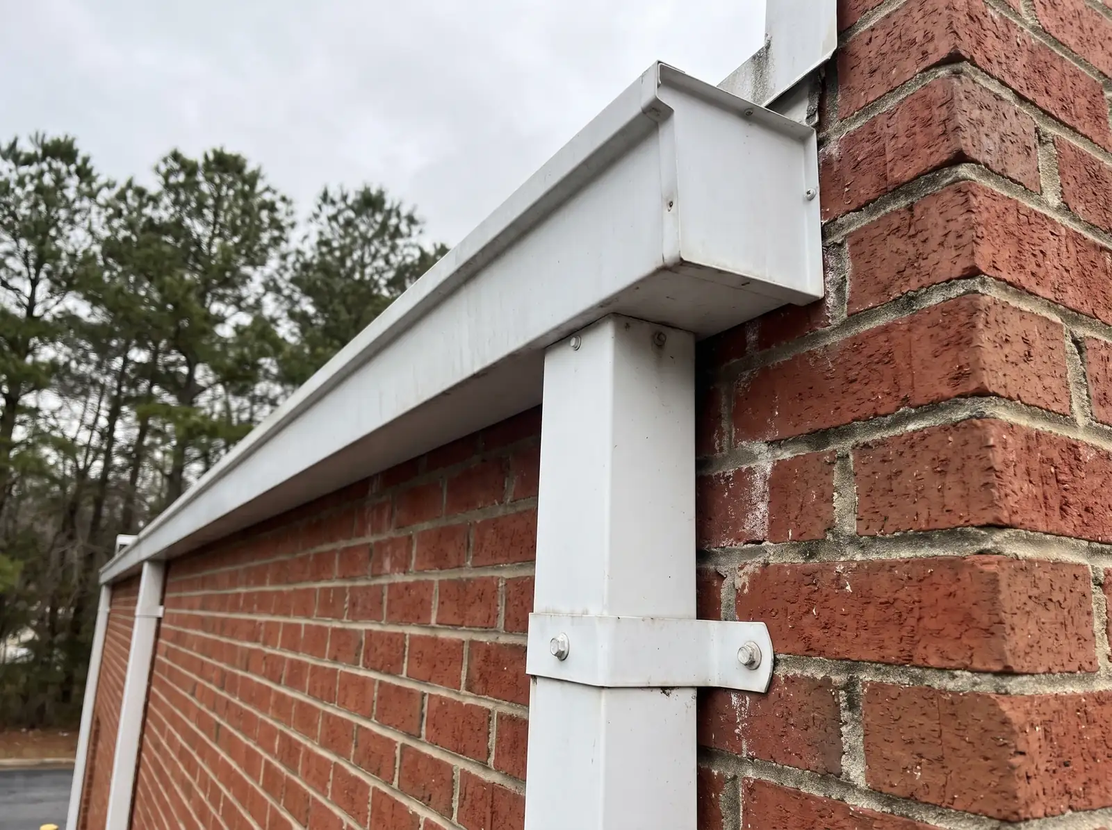 Large white box gutter and rectangular downspout strapped to a brick commercial wall