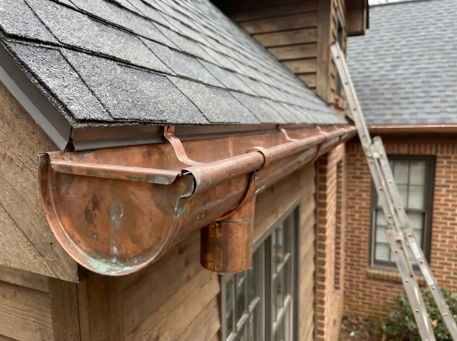 Half-round copper gutter and downspout outlet under the shingle edge of a house