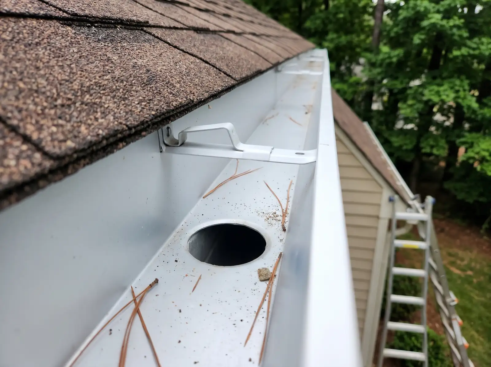 Clean white gutter with an open downspout outlet and a hidden hanger across the trough