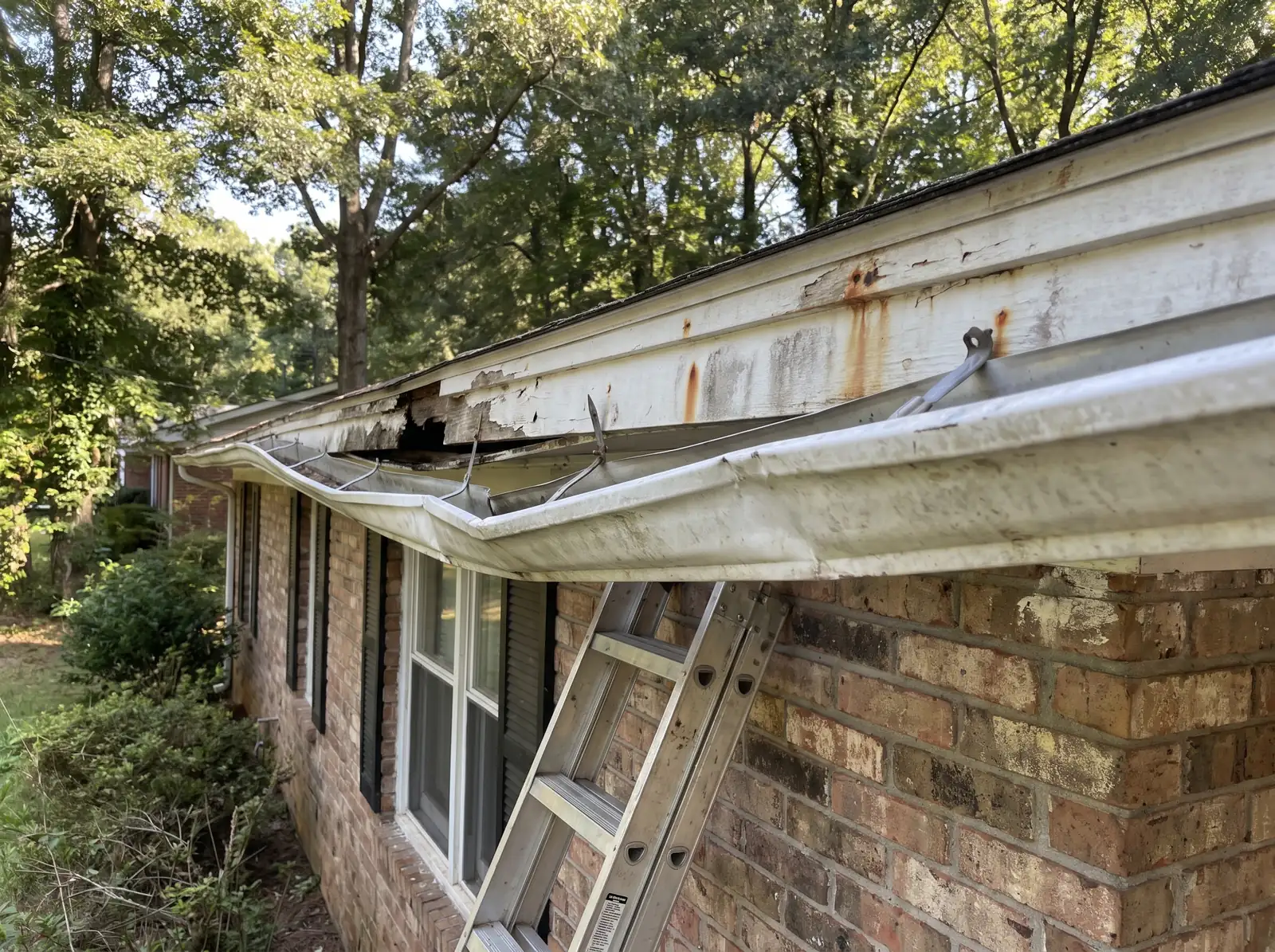 Old dented gutter sagging away from rust-stained fascia on a brick ranch house