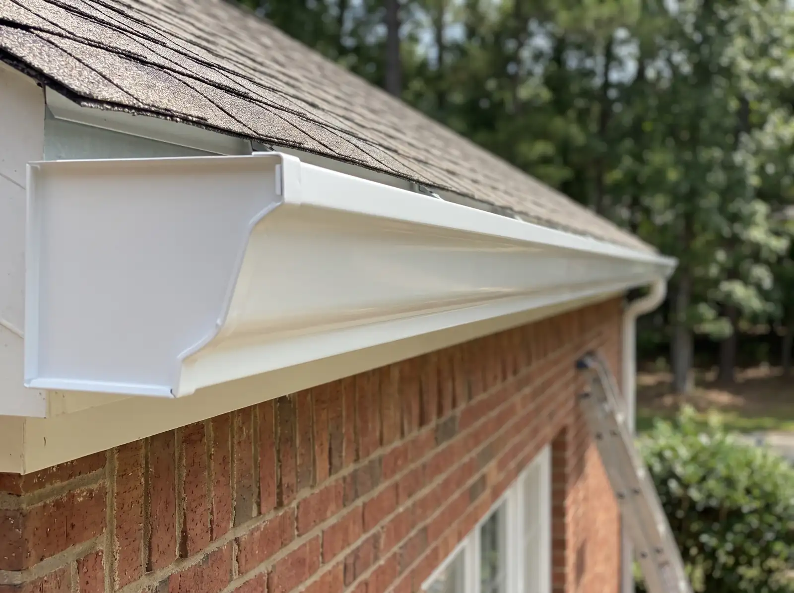 Long seamless white gutter with an end cap along the eave of a brick house